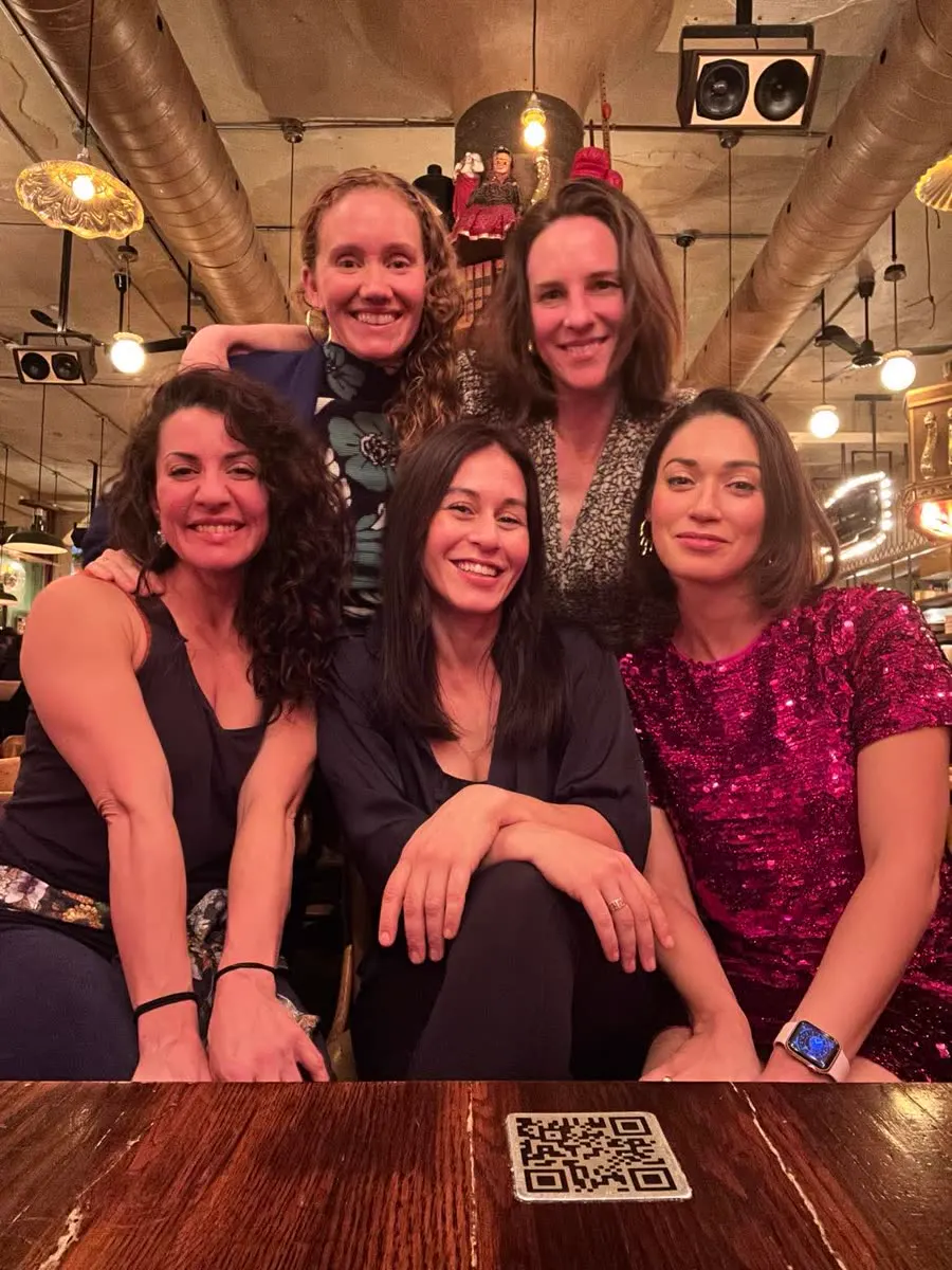 Five women pose together around a restaurant table