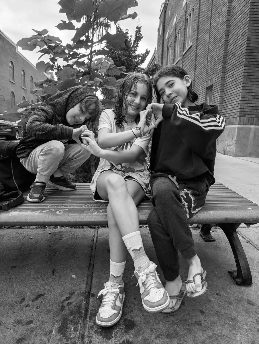 Three children on a bench form a heart with their hands, in black and white