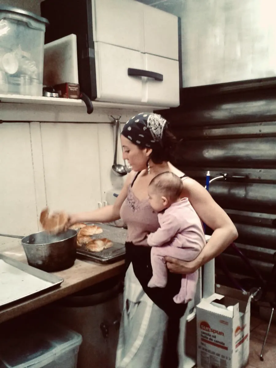 A staff member takes pastries out of the oven while holding a baby