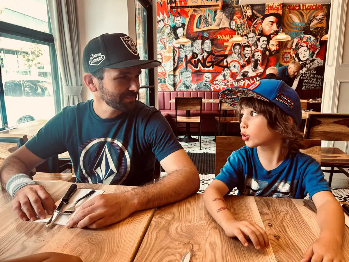 A man and a child at a restaurant table in front of a Portuguese mural