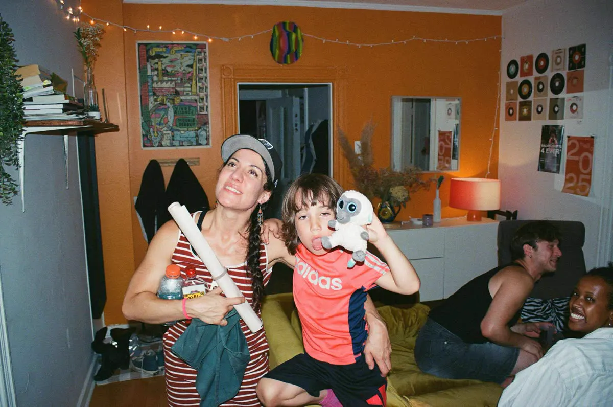 A woman holds a child in a living room with orange walls