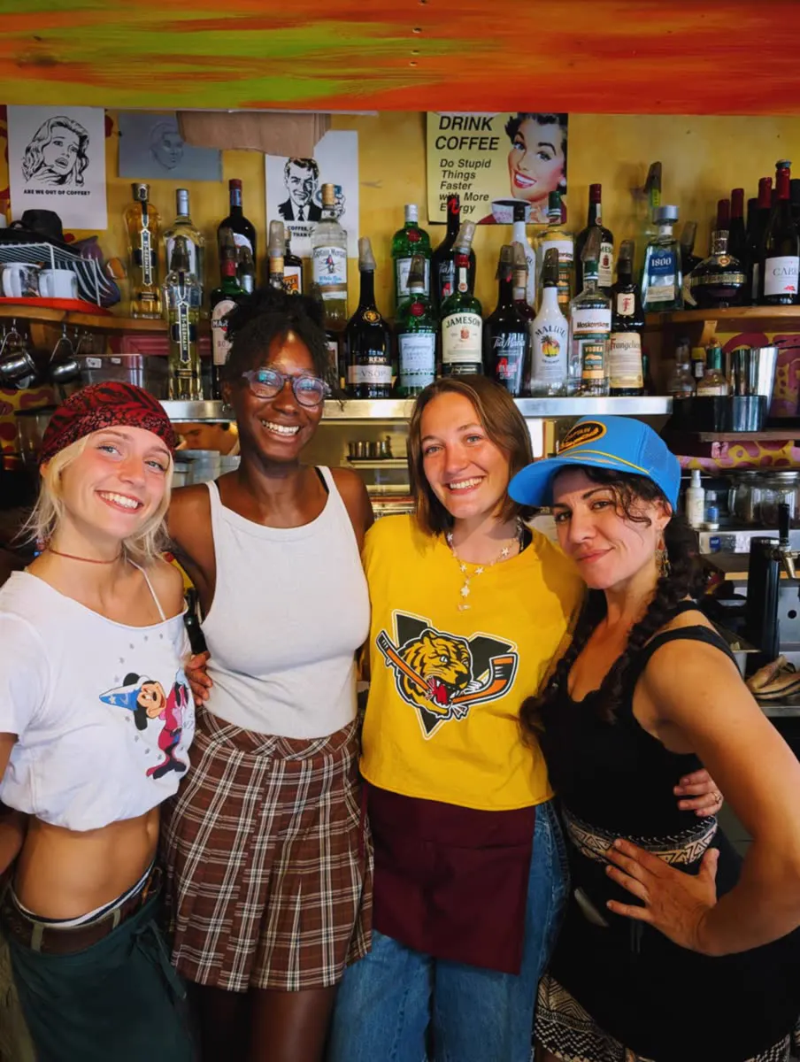 Four staff members pose behind the café bar, in front of the bottle shelves