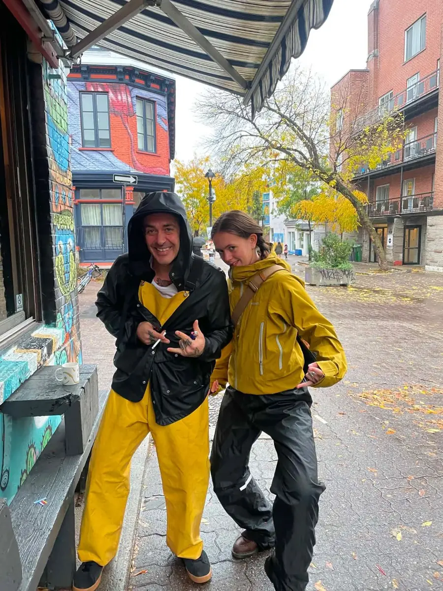 Deux membres de l'équipe en imperméables jaunes posent sous l'auvent du café, un jour de pluie